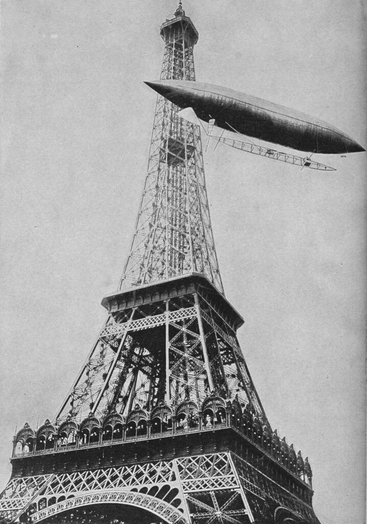 Black and white photograph of an airship circling the Eiffel Tower. 