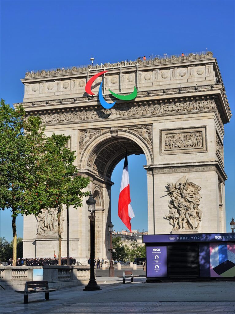 Photograph of the Paralympic logo on the top of the Arc de Triomphe with the French flag visible through the arch of the monument. 